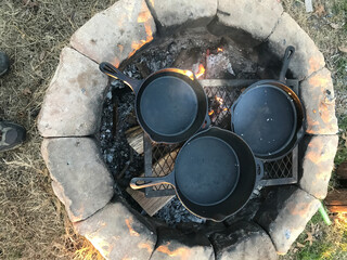cast iron skillets warming up over an open camp fire
