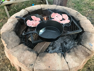 Pork chops cooking in cast iron skillets over an open flame