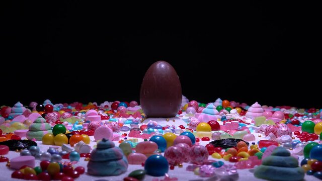 Easter confectionery and chocolate egg in the middle. Variety of holiday sweets, lollipop, candy beans, marshmallows, colorful gummy, sugar dessert, caramels, stripes, swirls, Liquorice on the table.