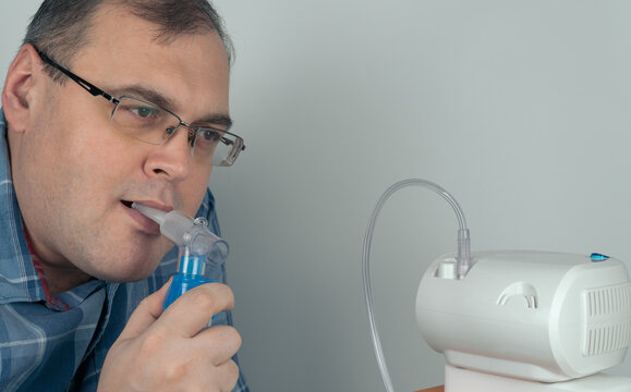 man with glasses holds a breathing mask and inhales. spraying of a drug that is delivered to the patient through a breathing tube. nebulizer and Oxygen Mask.