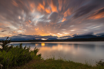 Long exposure calm sunrise from a lake with reflections on water during spring, with orange clouds and mountains on the background, Lake Koocanusa, British Columbia, Canada 