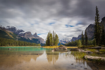 Long exposure landscape of Rocky mountains reflected on clear and green lake water with spruce and pine trees under a cloudy sky, Spirit Island, Maligne Lake, Jasper National Park, Alberta, Canada