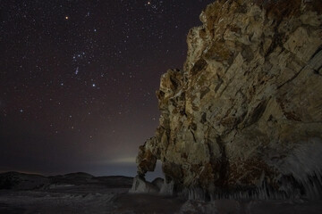 Rock with a stone arch on the shore of Lake Baikal and the constellation Orion