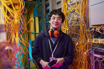 Waist up portrait of young network technician smiling at camera while standing in server room, copy...