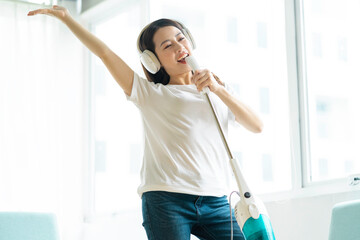 Asian woman listening to music and dancing with a vacuum cleaner