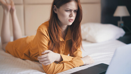 woman in dormitory on bed with laptop displeased facial expression work