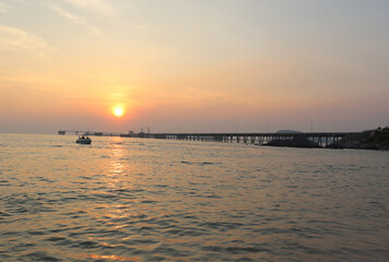 cement bridge in the sea for boats to dock and have the sunset in the evening. There is the shadow of the sun in the calm sea It gives a feeling of comfort and relaxation on vacation. in Thailand.