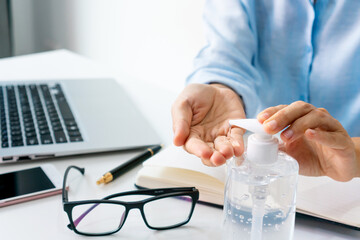 Asian businesswoman working at workplace and applying hand sanitizer gel on table during the...