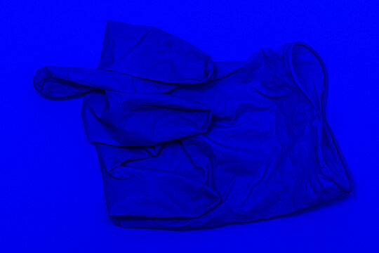 blue medical glove on a blue background the fingers are curled up in a kukish gesture