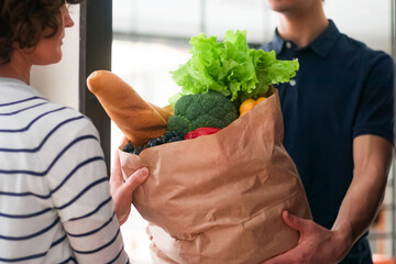 Food delivery. A man passes a paper bag with groceries to a woman.