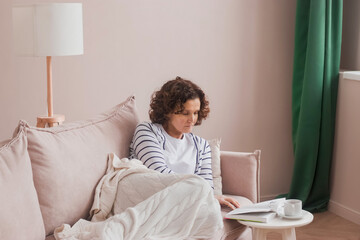 A woman reads a book lying on a sofa at home