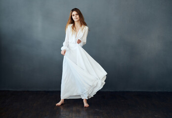 Fototapeta premium Red-haired Woman in a white dress in full growth on a gray background indoors