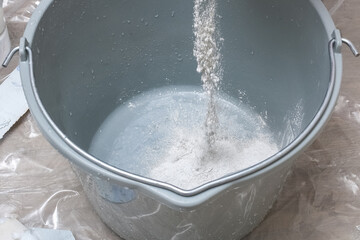 Mixing white plaster in a bucket with a stirrer. Close-up.