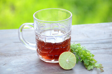 the black lemon tea in the glass cup with anise and lemon on the brown green background.