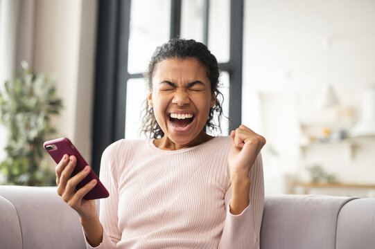 African American beautiful woman is surprised by what she saw on the phone, got message, passed the exam successfully, hired, got a visa, excited by news on smartphone, invited on a date, eyes closed