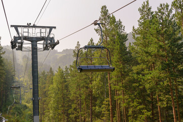 A detachable chairlift or high-speed chairlift is a type of passenger aerial lift. Ski lift in the summer season. Moving wire rope. Green pine forest in the mountains.