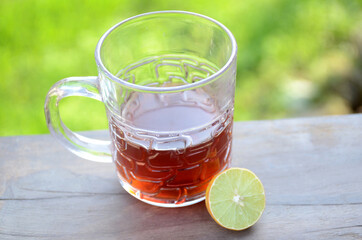the black lemon tea in the glass cup with lemon on the brown green background.