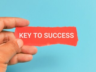 Phrase KEY TO SUCCESS on red strip paper hand held isolated on blue background.