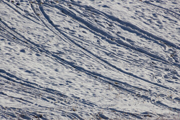 Many footprints, ski and sled tracks on a slope in the snow