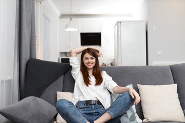 smiling woman sitting on the sofa with pillows comfortable apartment free time