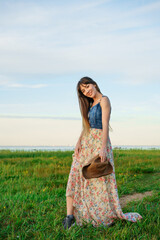 Beautiful happy young woman loose in a dress on nature and wearing a hat