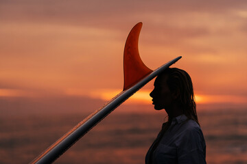 Beautifull woman on tropical beach holding surfboard at sunset in Bali
