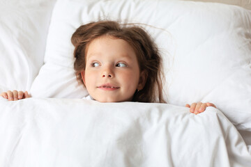 Cute child little girl woke up and lies in the bed.