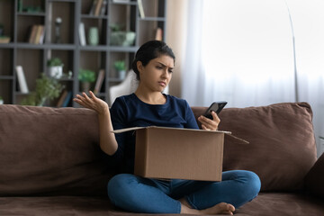 Upset Indian female buyer unbox package shopping online on smartphone confused with bad quality delivery service. Unhappy ethnic woman frustrated by wrong order buying on internet. Shipping concept.