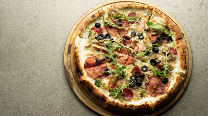 Ready-made round Italian pizza with cheese, salami and olives on a round wooden board on a gray background.