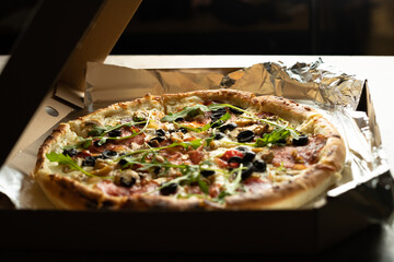 Pizza with olives and cheese in a delivery box on foil. Homemade baking.