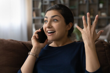 Stunned millennial Indian woman relax at home feel shocked talking on smartphone gadget. Happy...