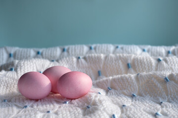 Three pink Easter eggs on a white knitted blanket