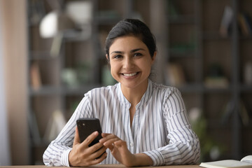Portrait of smiling young Indian woman client or user hold modern smartphone gadget shopping online. Happy millennial mixed race female use cellphone texting messaging on web. Technology concept.