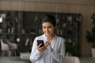 Happy Indian young woman hold modern cellphone text message online on gadget. Smiling mixed race ethnicity female client browse wireless internet on smartphone device. Technology concept.