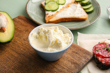 Bowl with tasty cream cheese on color wooden background