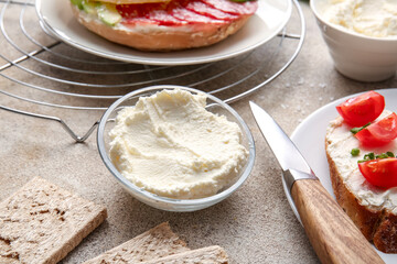 Bowl with tasty cream cheese on light background
