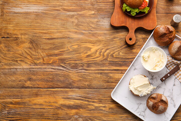 Bun and bowl with tasty cream cheese on wooden background