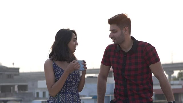 Front close up view of a smiling couple having coffee or tea while talking to each other,enjoying time together with coffee.Two best friends happily talking while standing on roof,having fun together
