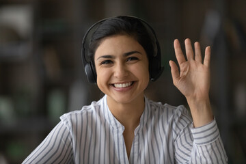 Close up screen view headshot portrait of happy millennial Indian woman in headphones talk on video...