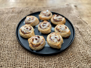 Homemade Cinnamon Rolls or Cinnamon Buns Pouring Cream Sauce on Wooden Surface.
