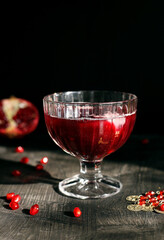 Ruby red pomegranate juice in a glass with ice on a rustic dark mystical background