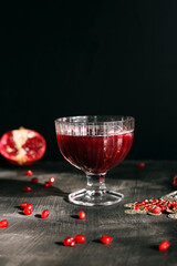 Ruby red pomegranate juice in a glass with ice on a rustic dark mystical background