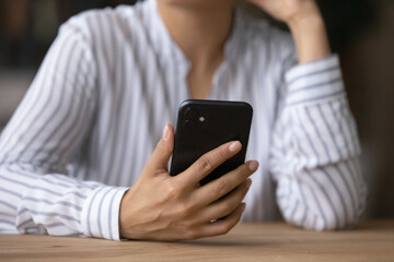 Crop close up of ethnic woman sit at desk use modern cellphone gadget browse wireless internet. Indian female hold smartphone text message online, have video call on cell webcam. Technology concept.