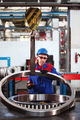 A worker in overalls and a hard hat moves a large-diameter bearing using a crane. Bearing plant....