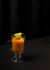 Glass of orange juice with lime on a dark background. Modern composition, copy space.