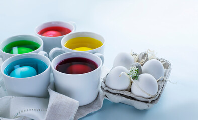 Easter eggs dye process and eggs in carton over light blue background. Image with copy space