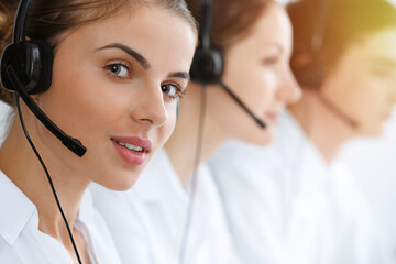 Call center. Beautiful young woman using headset and computer to help customers in sunny office. Business concept