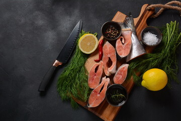 Fresh raw salmon steaks on board with salt, peppers, lemon,  on black background,