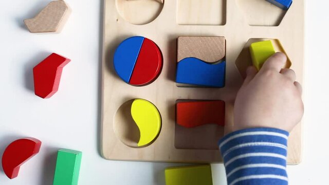Educational toys, Cognitive skills, Montessori activity. Closeup: Hands of a little Montessori kid learning about color, shape, sorting, arranging by engaged colorful wooden sensorial blocks. 