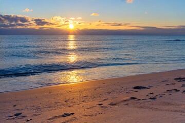 Golden rays of the setting sun are reflected on the water surface of the sea and the sandy shore on which traces of people are visible